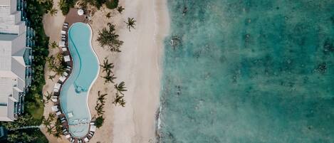 An aerial view of a resort with a swimming pool, beach, and palm trees.