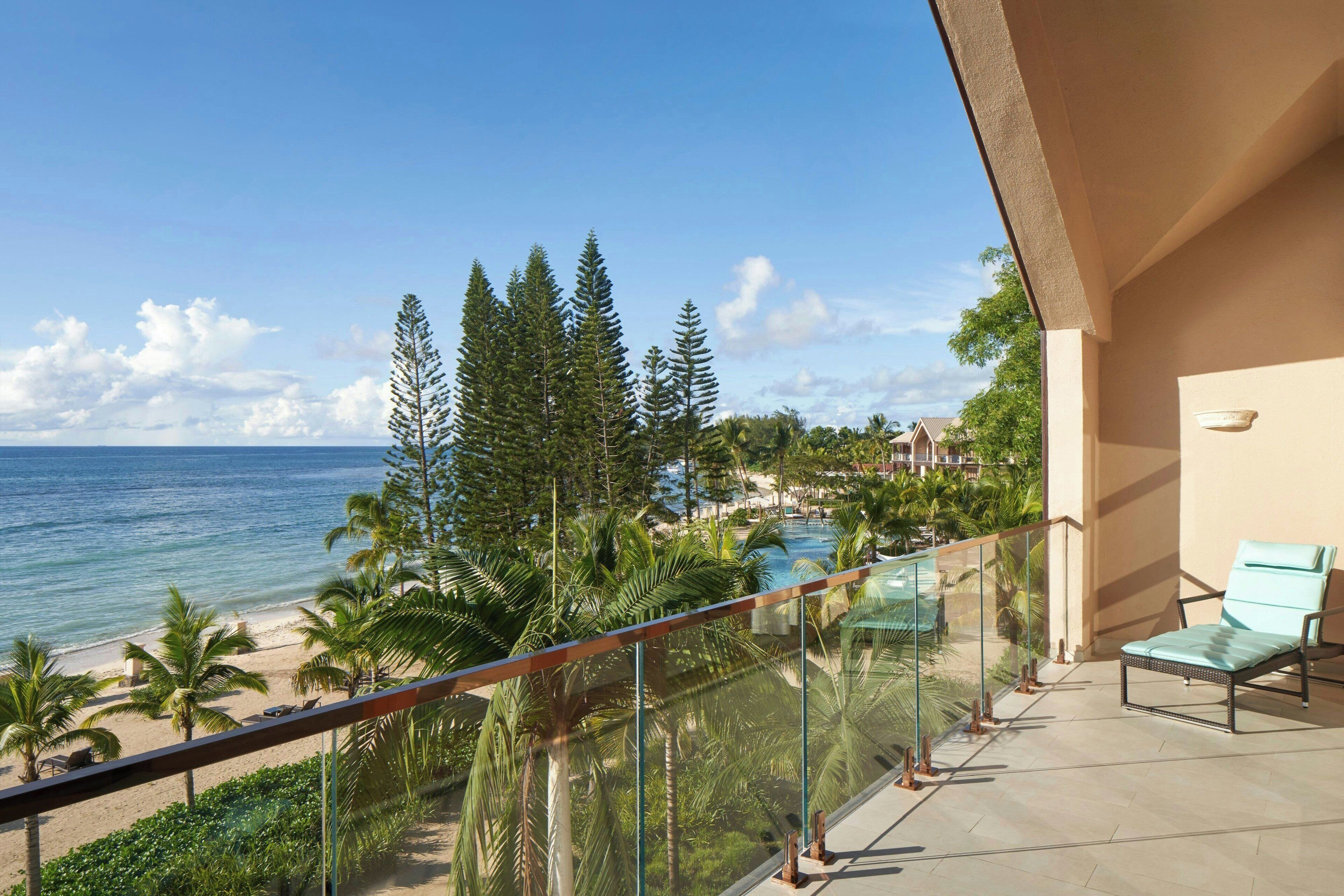 A balcony with a clear view of the beach, palm trees, and a pool.