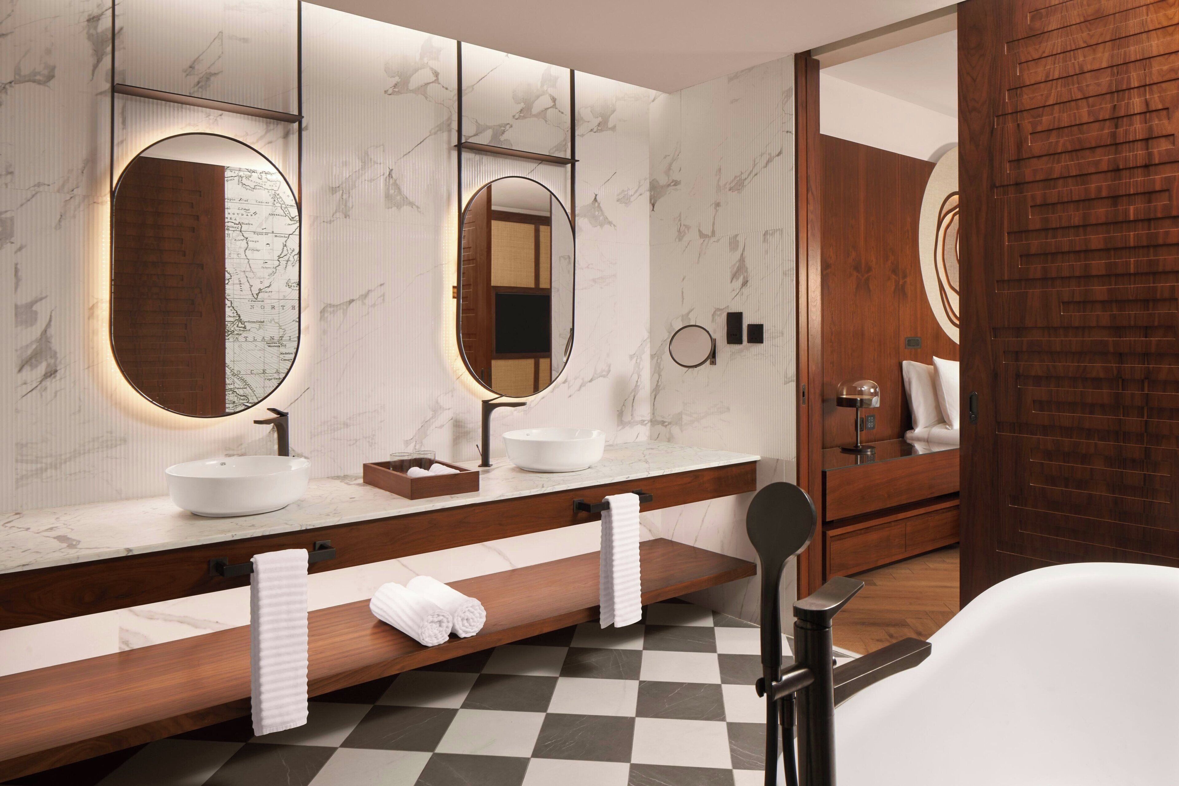 A modern bathroom with a large mirror, a white sink, and a wooden vanity.