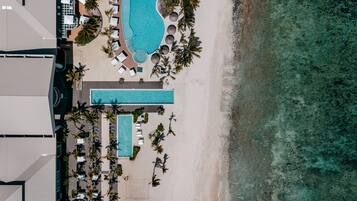 An aerial view of a resort with a large swimming pool, beach area, and lounge chairs.