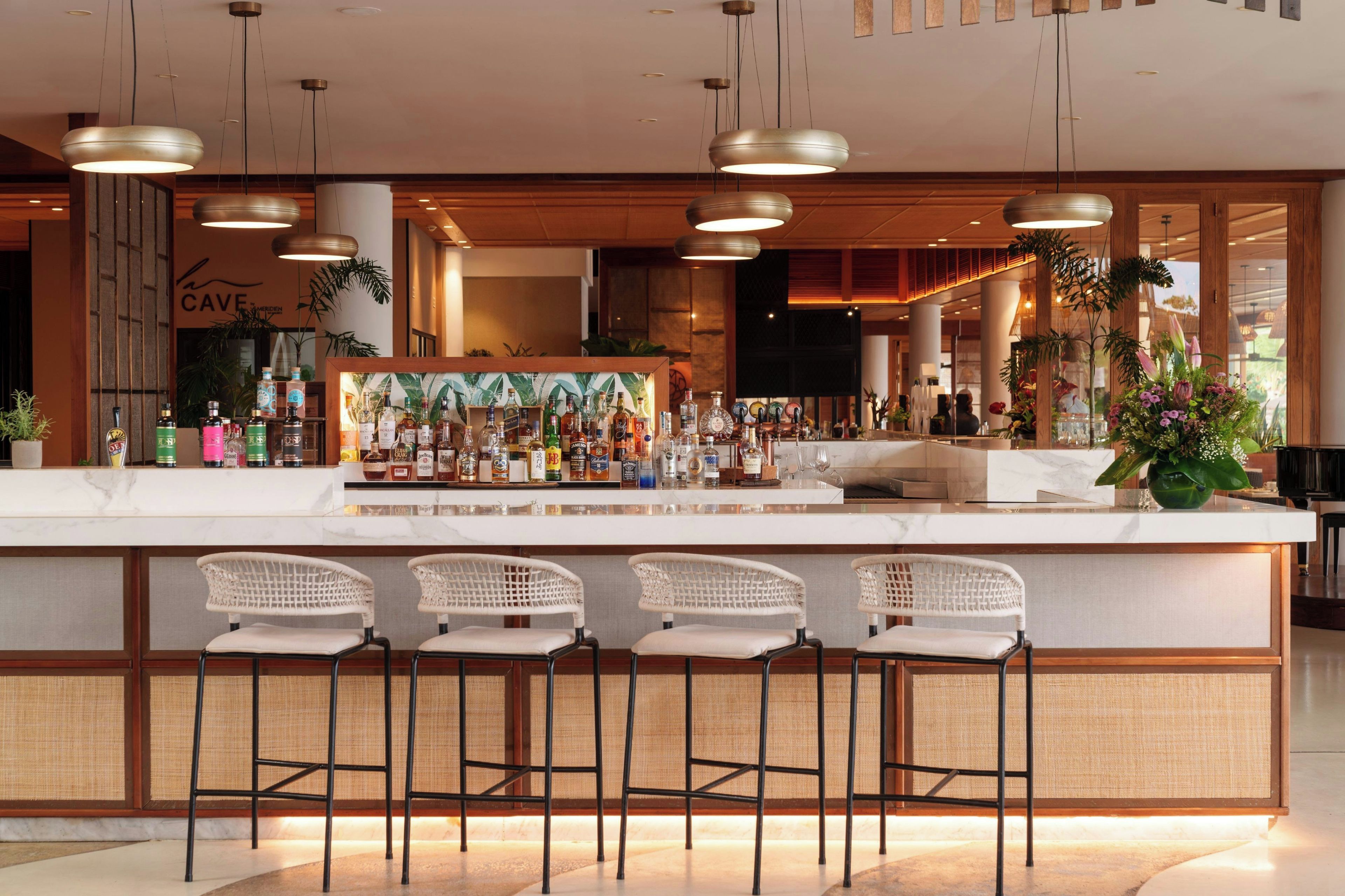 A bar area with a marble countertop, multiple liquor bottles, and three wicker bar stools.