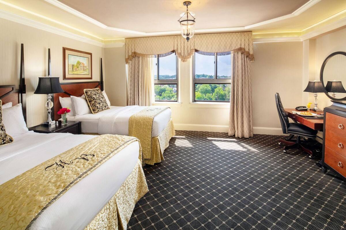 Ein Hotelzimmer mit zwei Betten, einem Schreibtisch, einem Stuhl, einem Schminktisch und einem großen Fenster mit Aussicht.