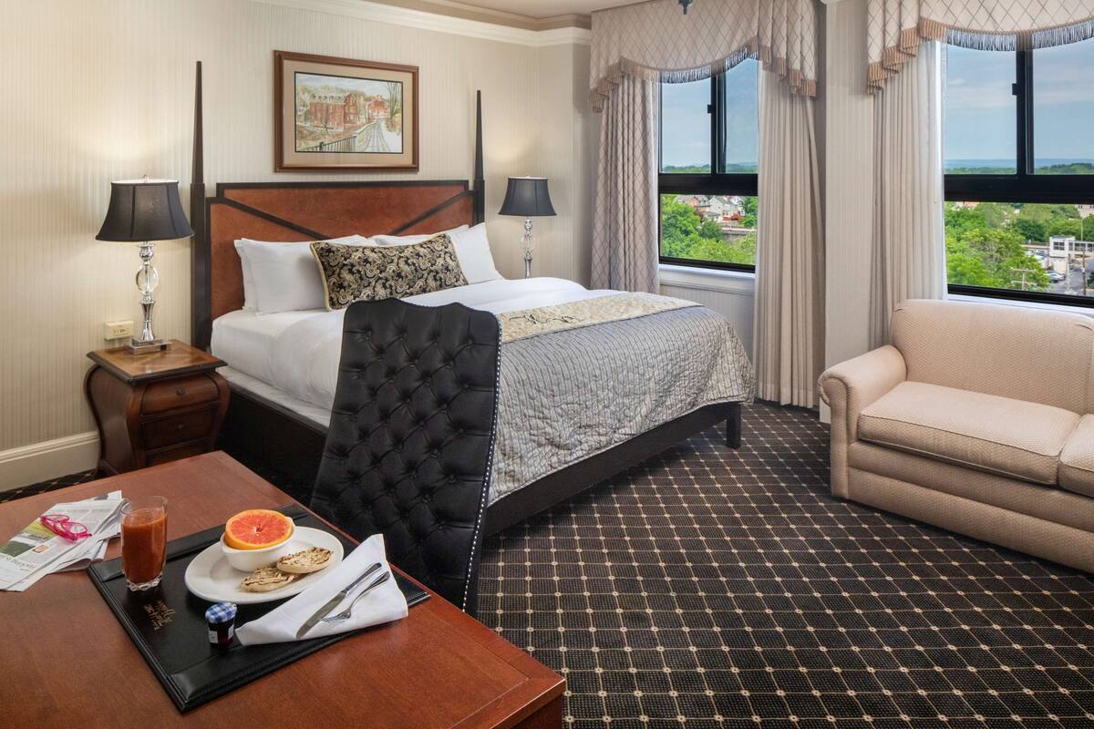 Ein Hotelzimmer mit Bett, Sofa, Frühstückstisch und Blick auf die Stadt.