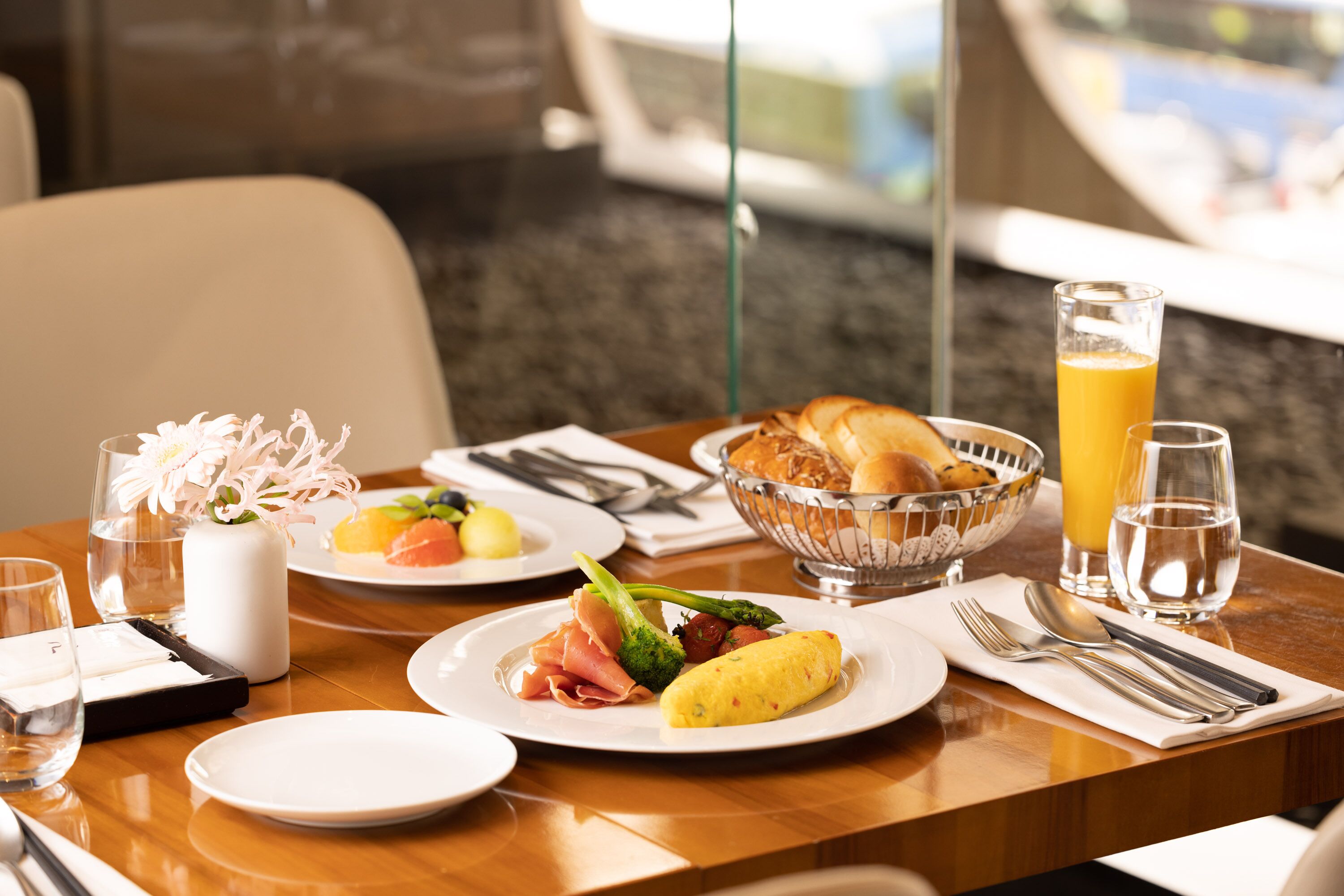 A breakfast table with plates of food, a glass of orange juice, and a bowl of bread.