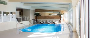 An indoor swimming pool with a water feature, sun loungers, and a view of the interior space.