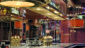 A bar area with multiple gold-colored dispensers, a variety of bottles, and a well-lit ambiance with overhead lighting fixtures.