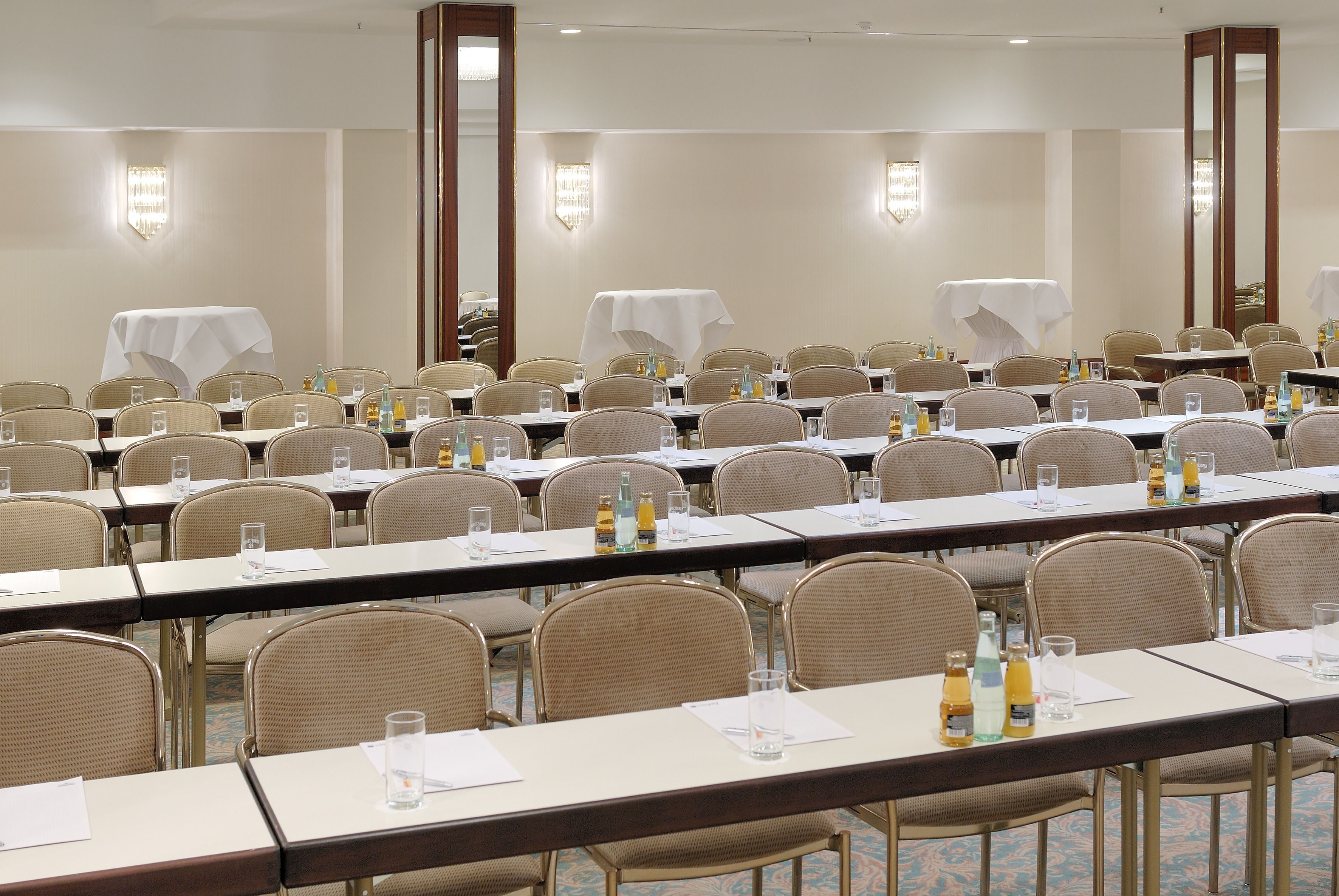 A conference room with multiple tables, chairs, and tables covered with white tablecloths.