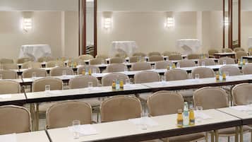 A conference room with multiple tables, chairs, and tables covered with white tablecloths.