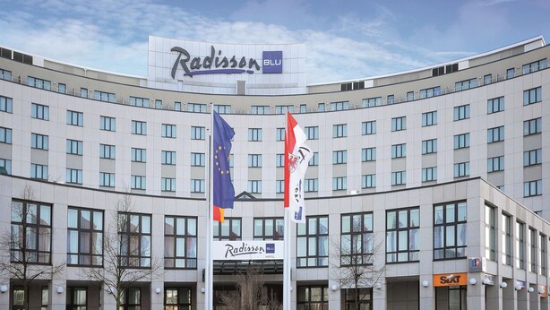 A Radisson Blu hotel with a curved facade, multiple windows, and flags including the European Union flag.