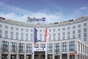Et Radisson Blu hotel med en buet facade, mange vinduer og flag, heriblandt EU-flaget.