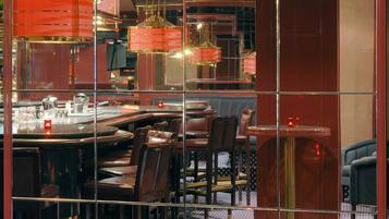 A restaurant with a mirrored wall, round tables, and cushioned chairs.