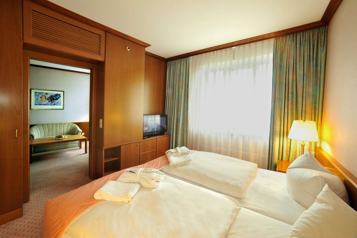 A hotel room with two beds, a television, a sofa, and a window with curtains.