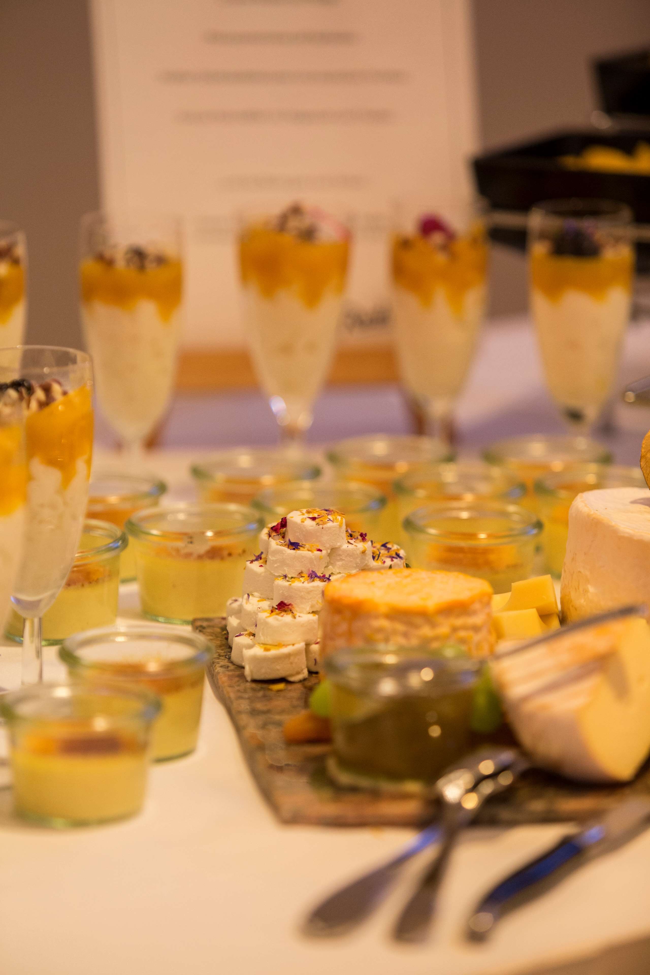 Una mesa con diversos alimentos, incluyendo queso y postres, dispuesta para una reunión.