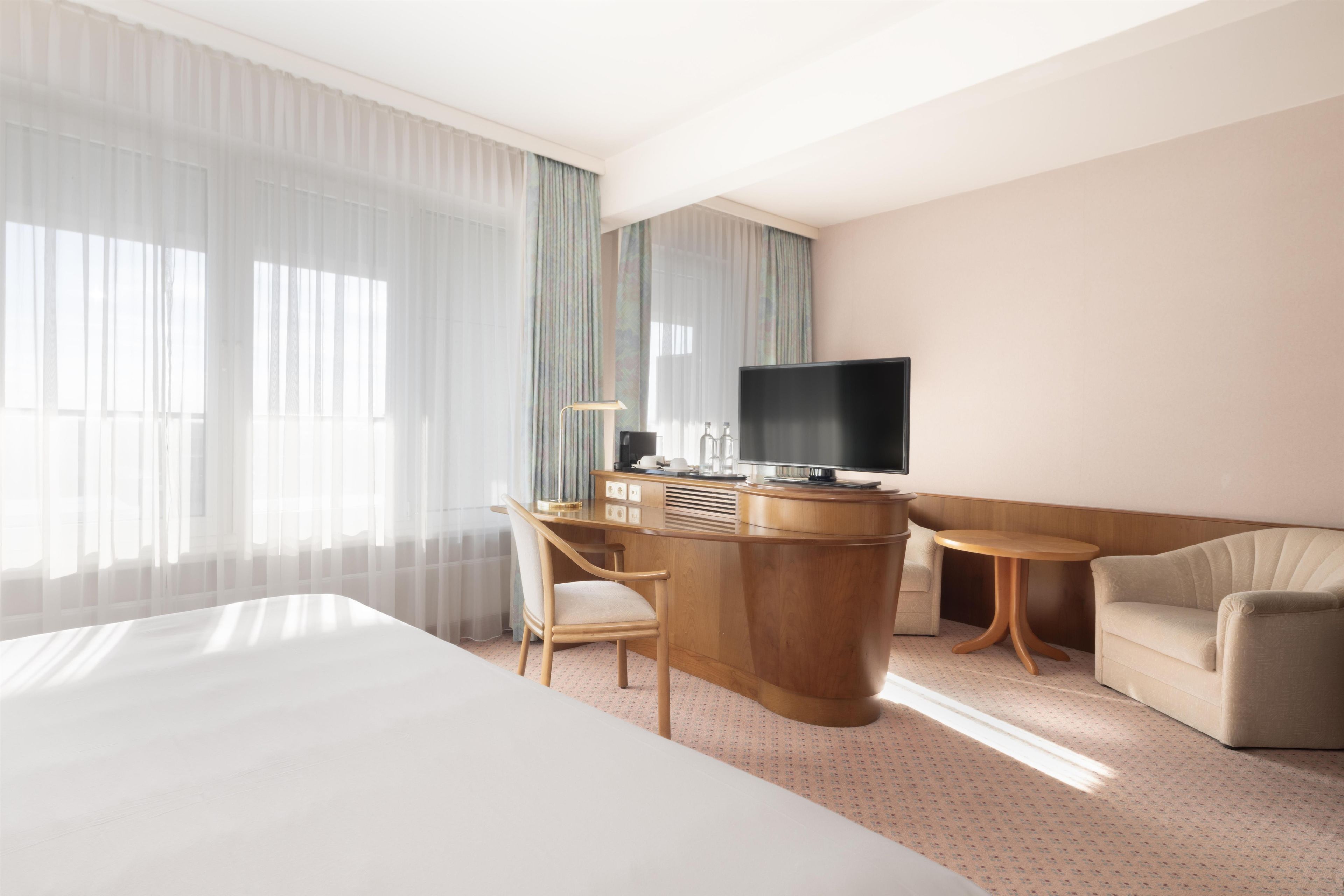 A hotel room with a bed, a desk with a television, a chair, and a sofa.