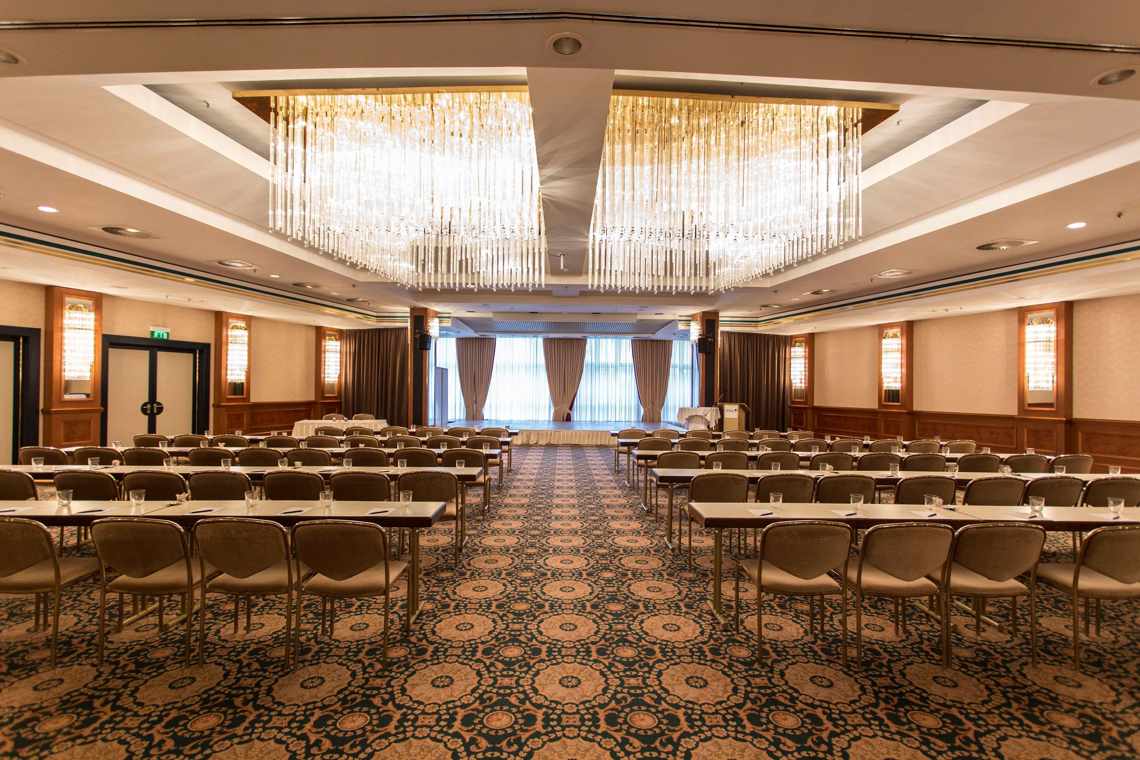 A conference room with rows of tables and chairs, a patterned carpet, and a large chandelier.