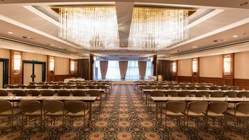 A conference room with rows of tables and chairs, a patterned carpet, and a large chandelier.