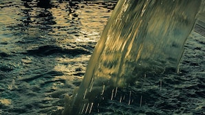A person standing by a window with a view of a waterfall and the sun setting.