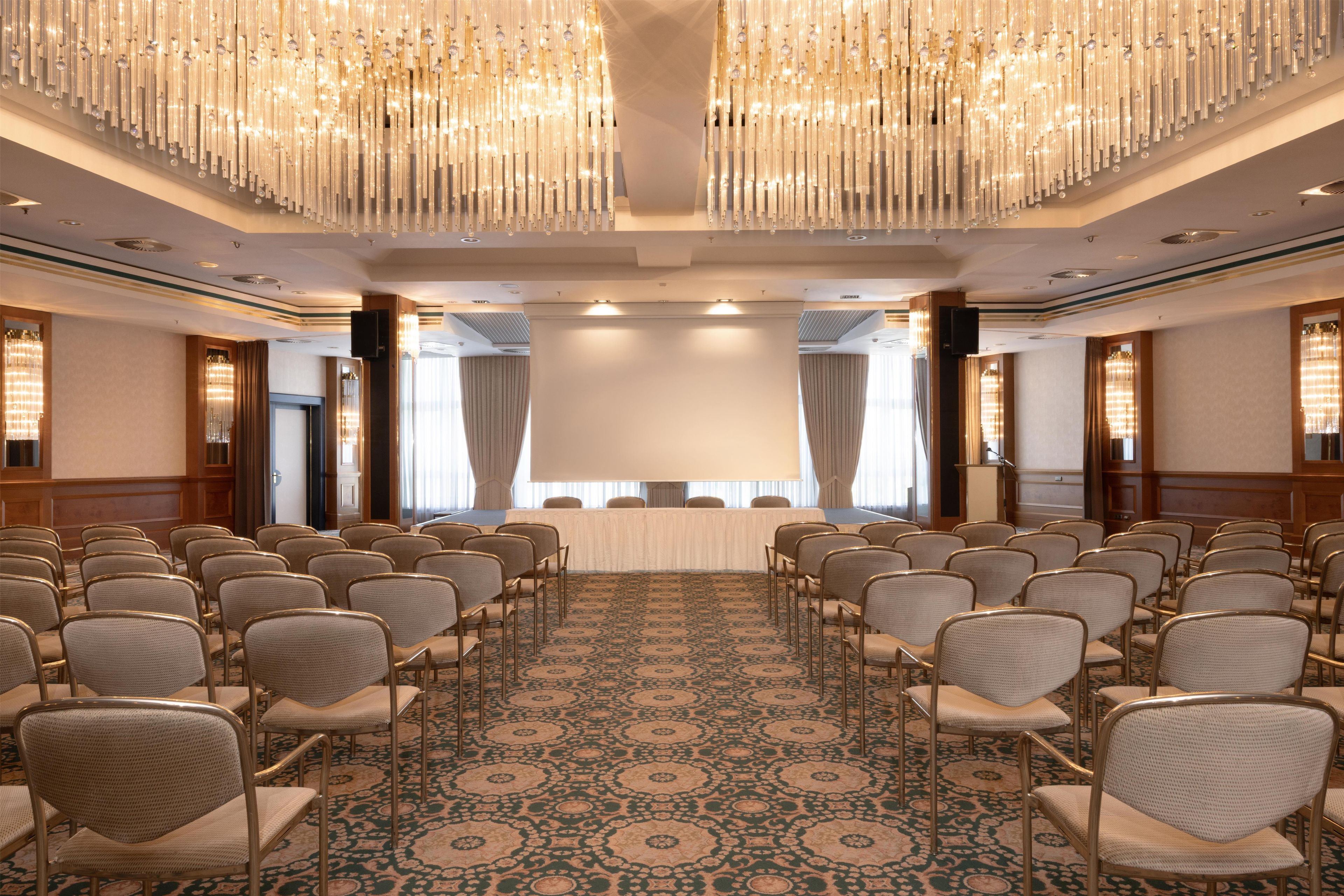 A conference room with rows of chairs, a large table, and a carpeted floor.