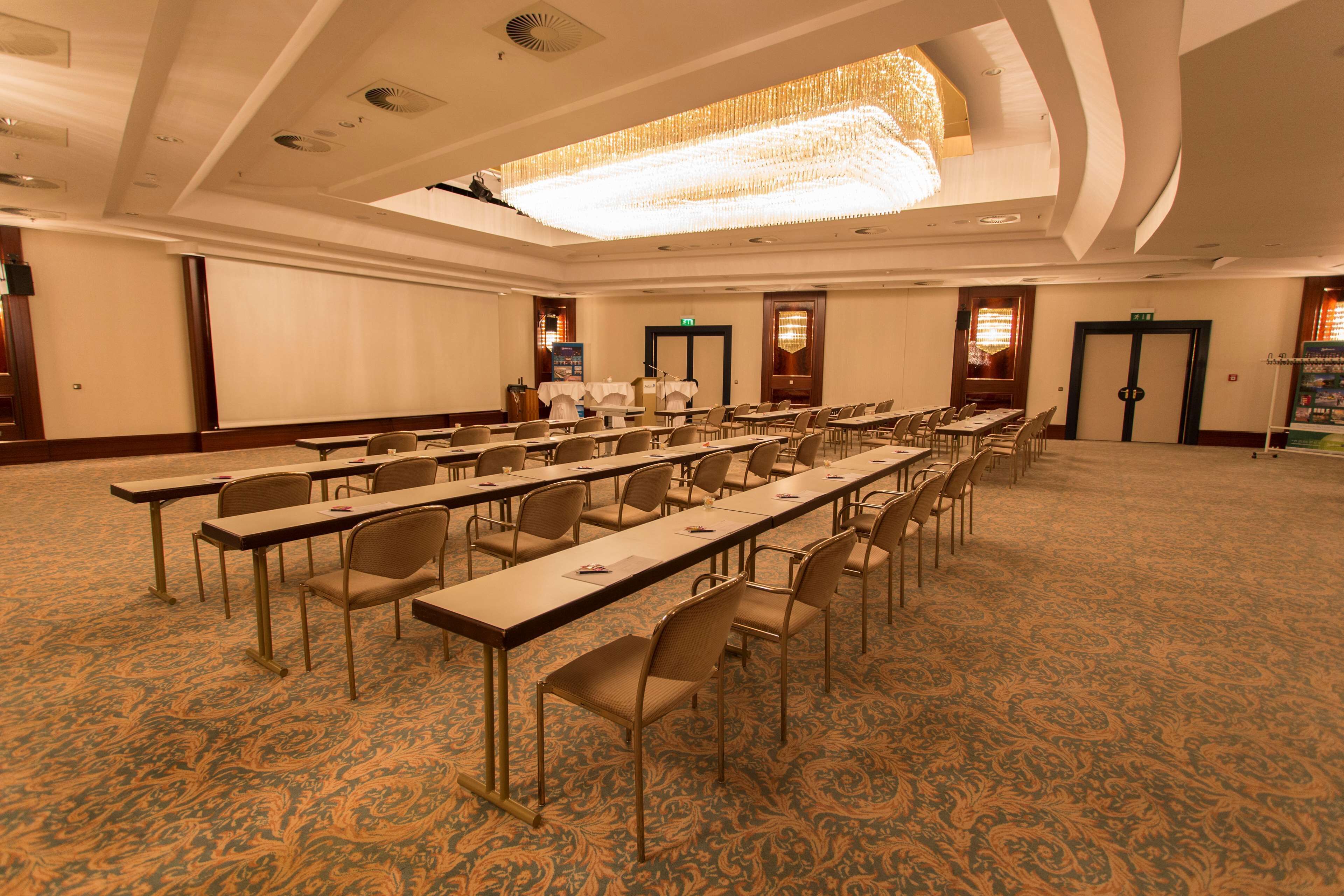 A conference room with long tables and chairs, a patterned carpet, and a chandelier.