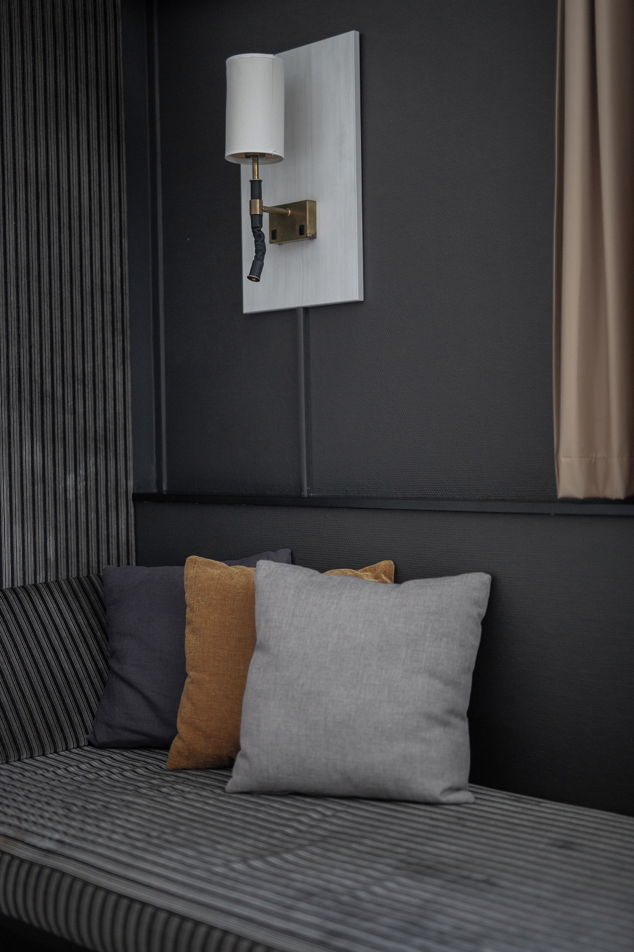 Un dormitorio moderno con pared oscura, una lámpara de noche y una cama con ropa de cama a rayas y tres almohadas.