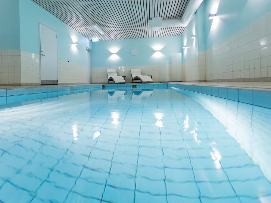 Una piscina con paredes y techo azulejados, dos sillas de descanso y una puerta.