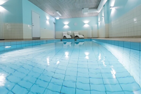 A swimming pool with tiled walls and ceiling, two lounge chairs, and a door. - Quality Hotel Royal Corner (Växjö)
