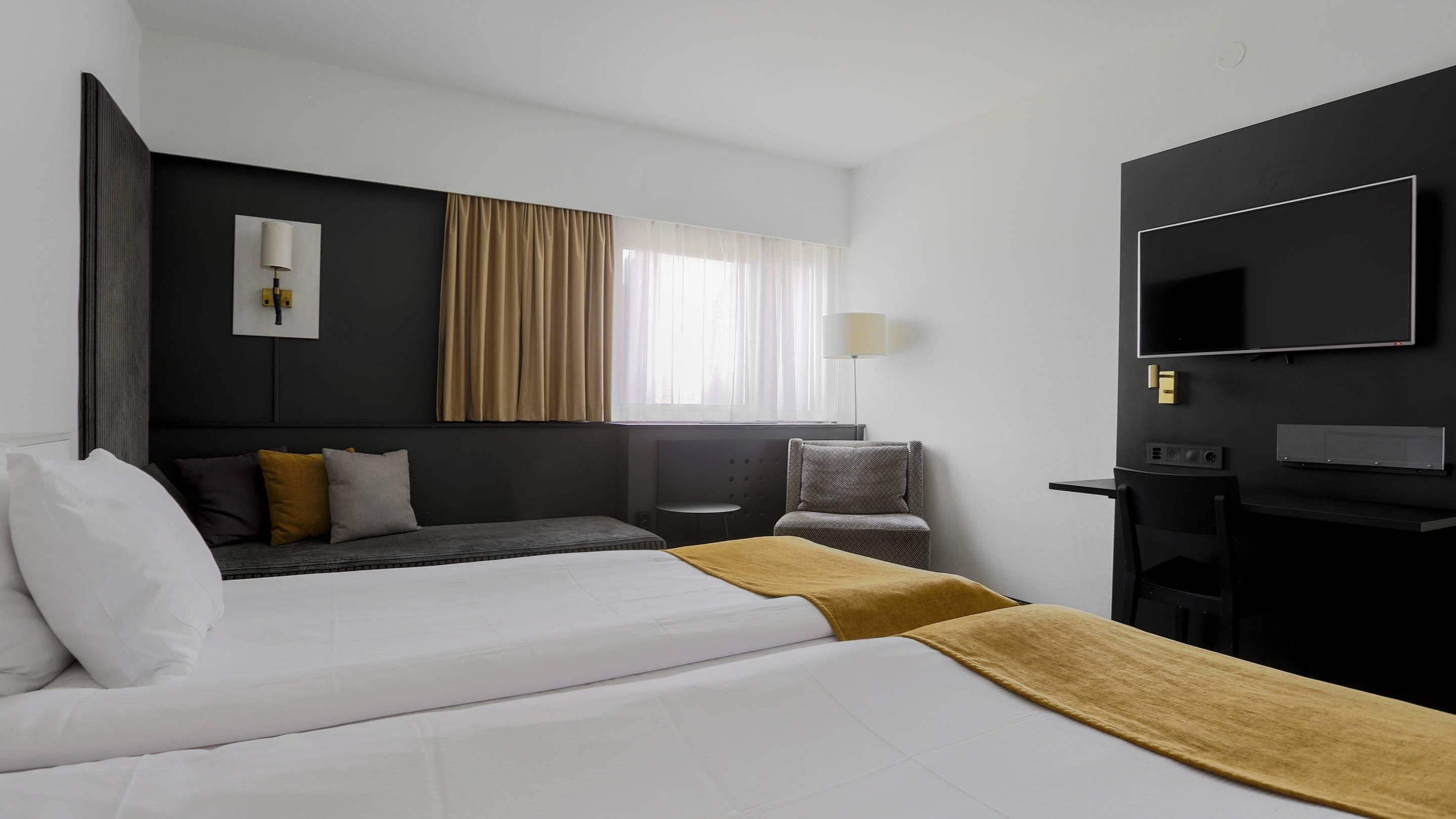 Ein Hotelzimmer mit einem Bett, einem Schreibtisch, einem Sessel, einem Fernseher und einem Fenster mit Vorhängen.