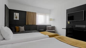 Ein Hotelzimmer mit einem Bett, einem Schreibtisch, einem Sessel, einem Fernseher und einem Fenster mit Vorhängen.