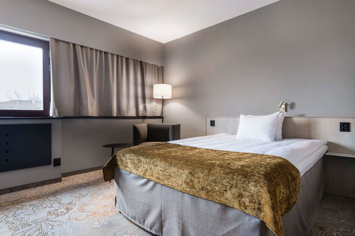 A hotel room with a bed, a desk, and a window with curtains.