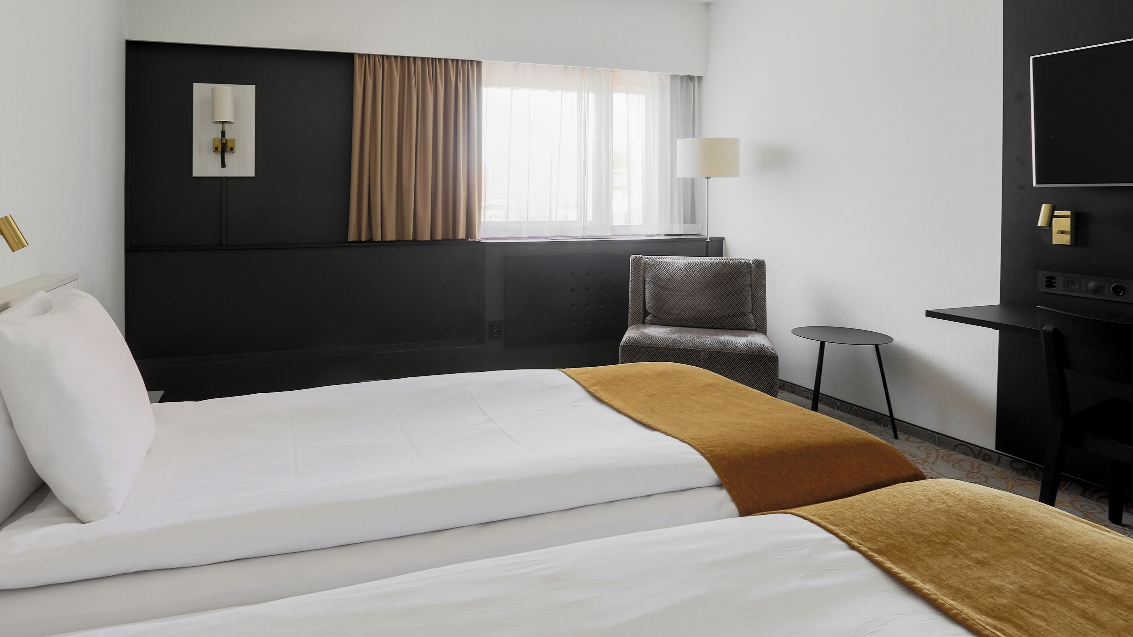 A hotel room with a large bed, a small armchair, a side table, and a television.