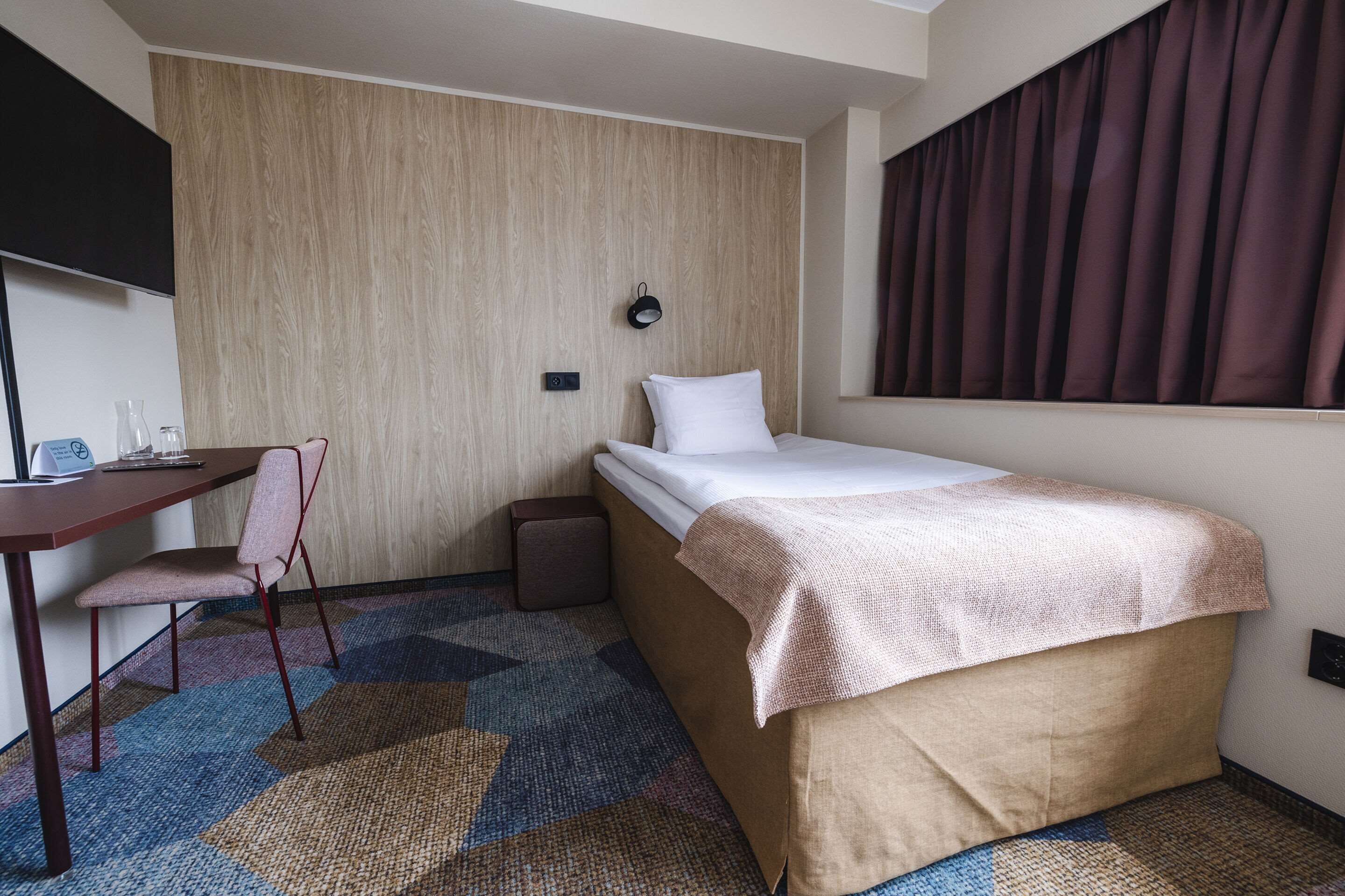 A hotel room with a bed, a desk, a chair, and a small table.