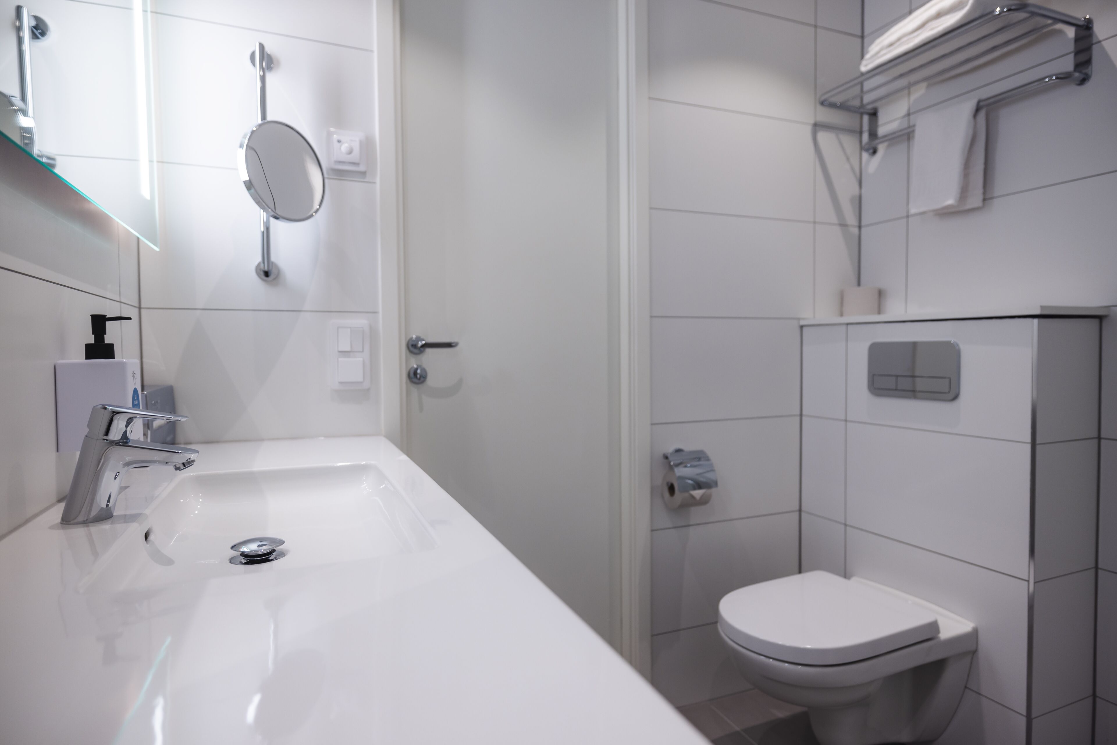 A modern bathroom with a white sink, mirror, and toilet.
