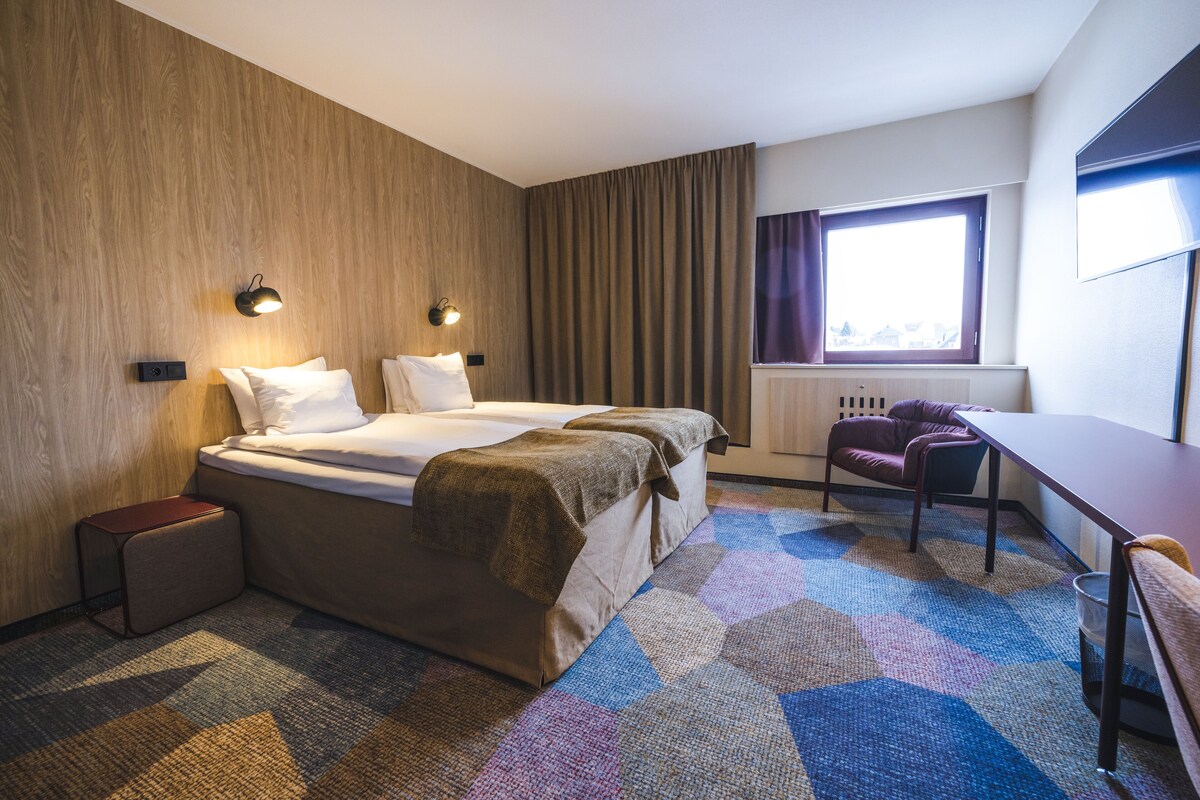 A hotel room with a large bed, a desk, and a window with curtains.