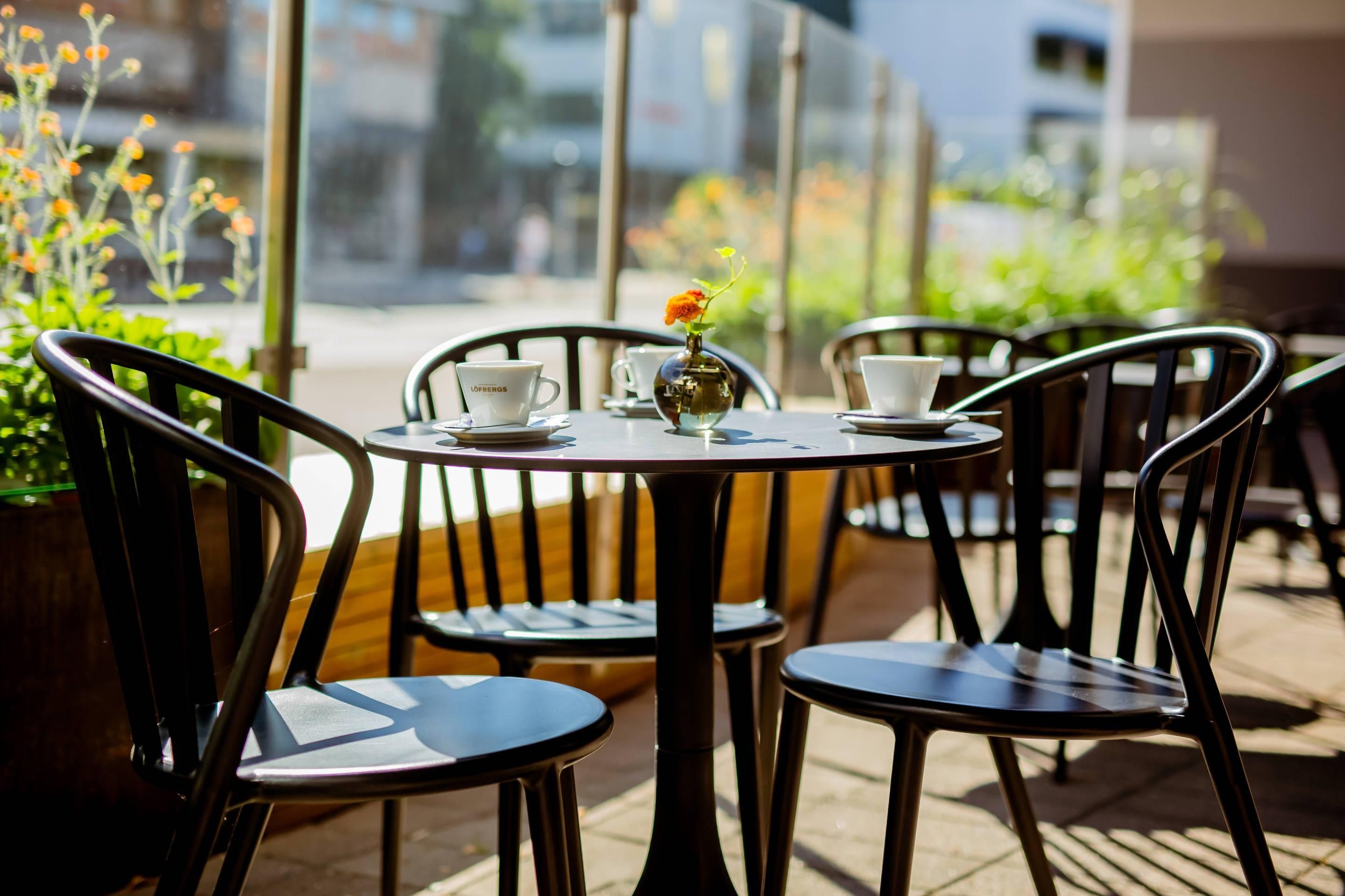 An outdoor café with round tables and chairs, a vase with flowers, and cups on the tables.