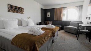 A hotel room with two beds, a sofa, a dining table, and a window with curtains.