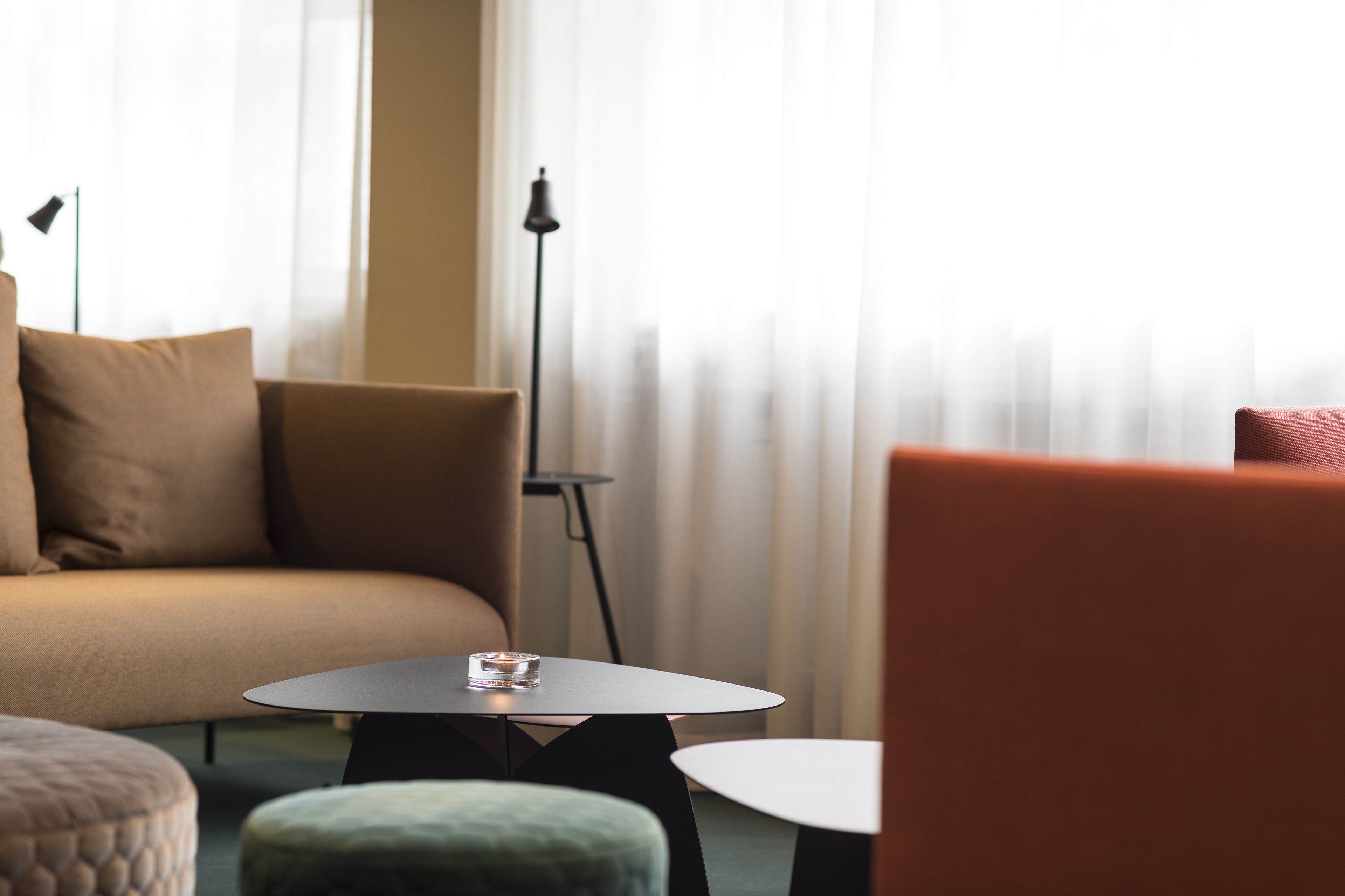 A modern living room with a sofa, ottoman, and a small table with a candle.