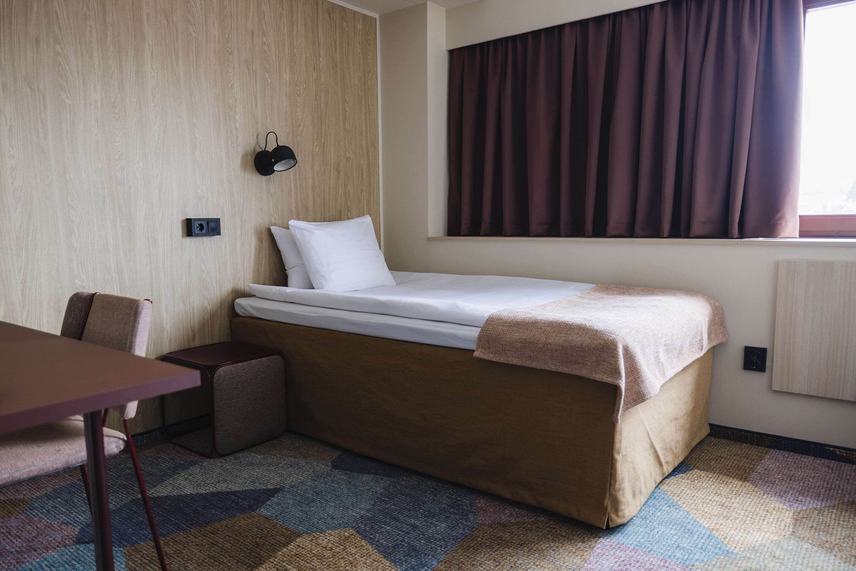 A small, neatly arranged hotel room with a single bed, a desk, and a chair.