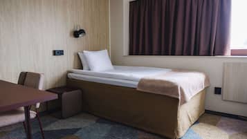 A small, neatly arranged hotel room with a single bed, a desk, and a chair.
