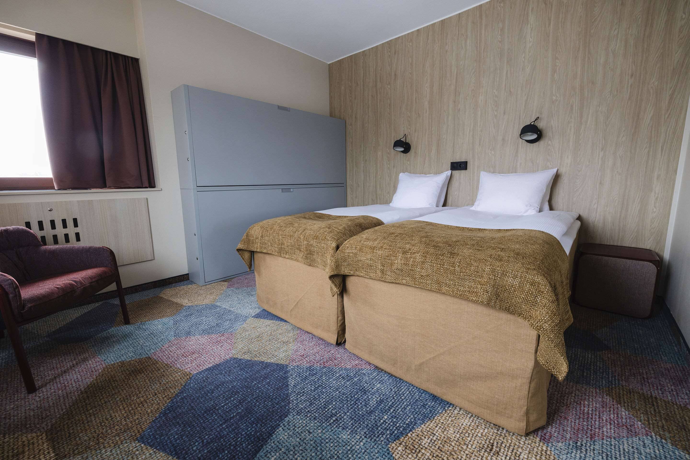 A hotel room with a bed, a wardrobe, a chair, and a window with curtains.