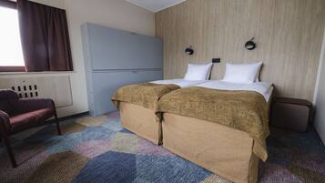 A hotel room with a bed, a wardrobe, a chair, and a window with curtains.