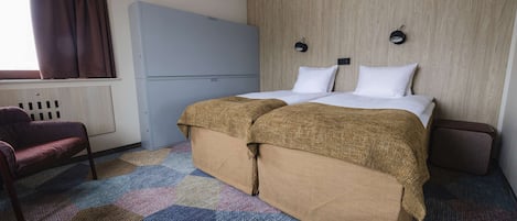 A hotel room with a bed, a wardrobe, a chair, and a window with curtains.