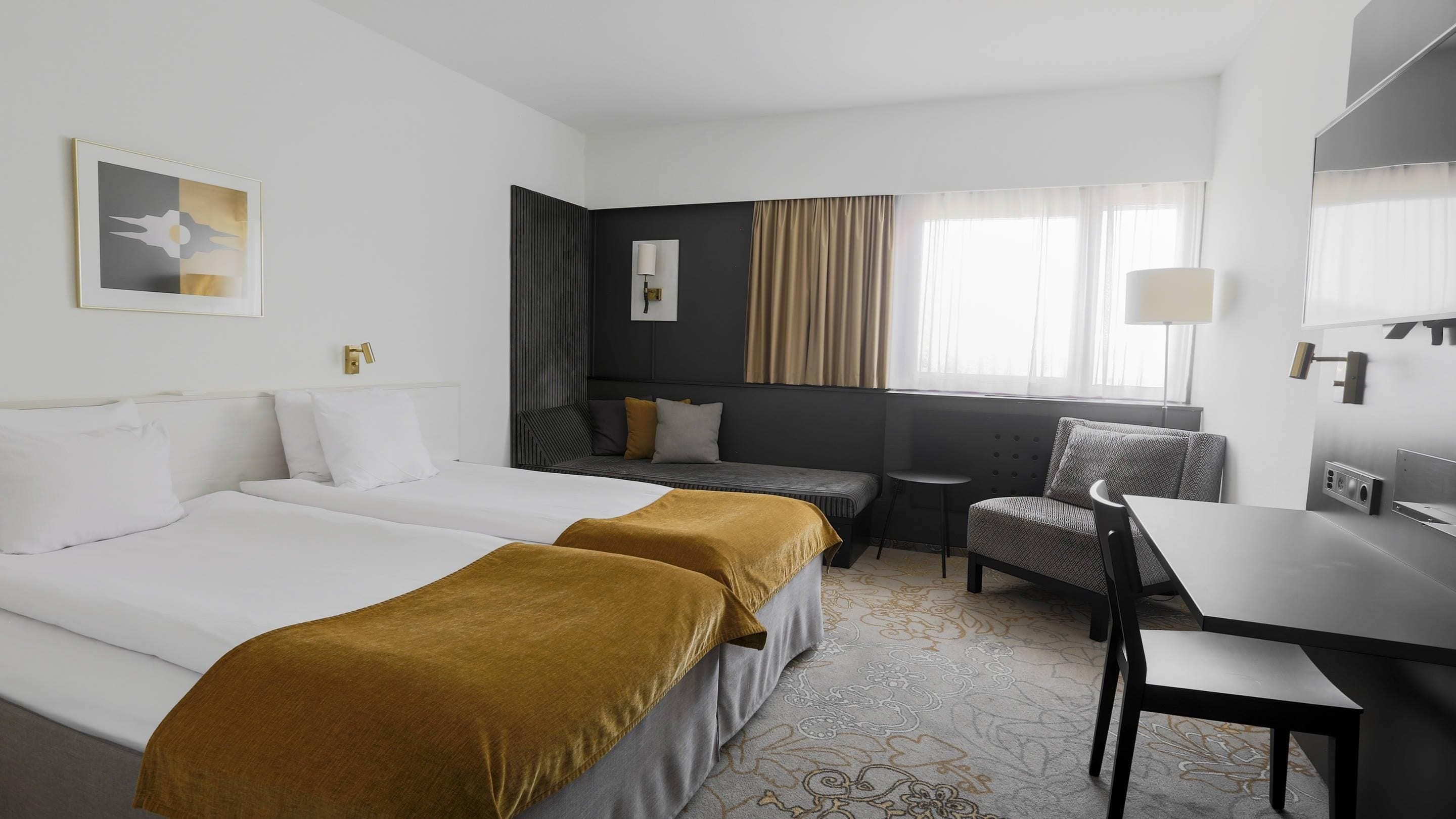 Habitación de hotel con dos camas, un escritorio, una silla, un sofá y una ventana con cortinas.
