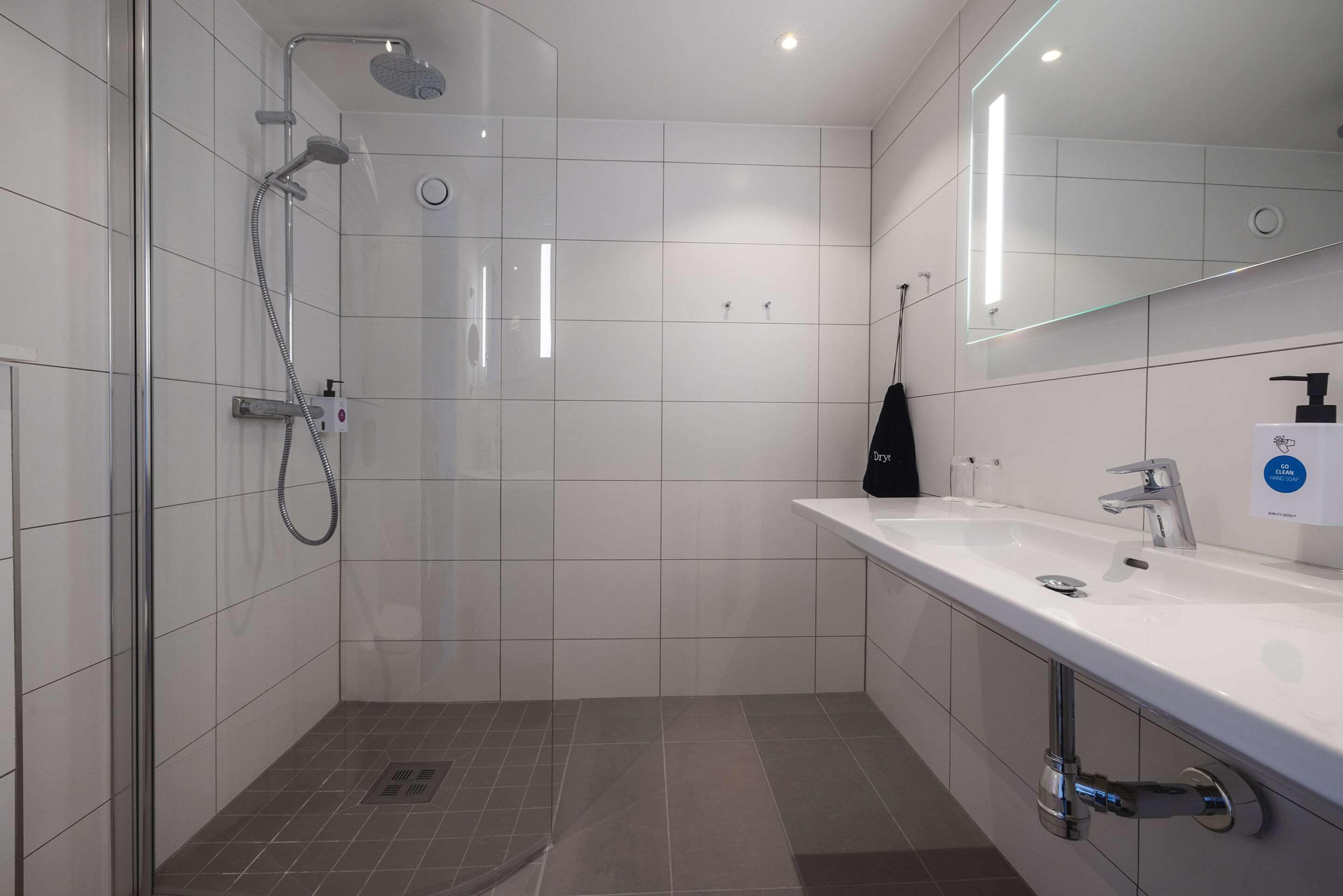 A modern bathroom with a glass-enclosed shower, a white sink with a mirror, and a black handheld showerhead.