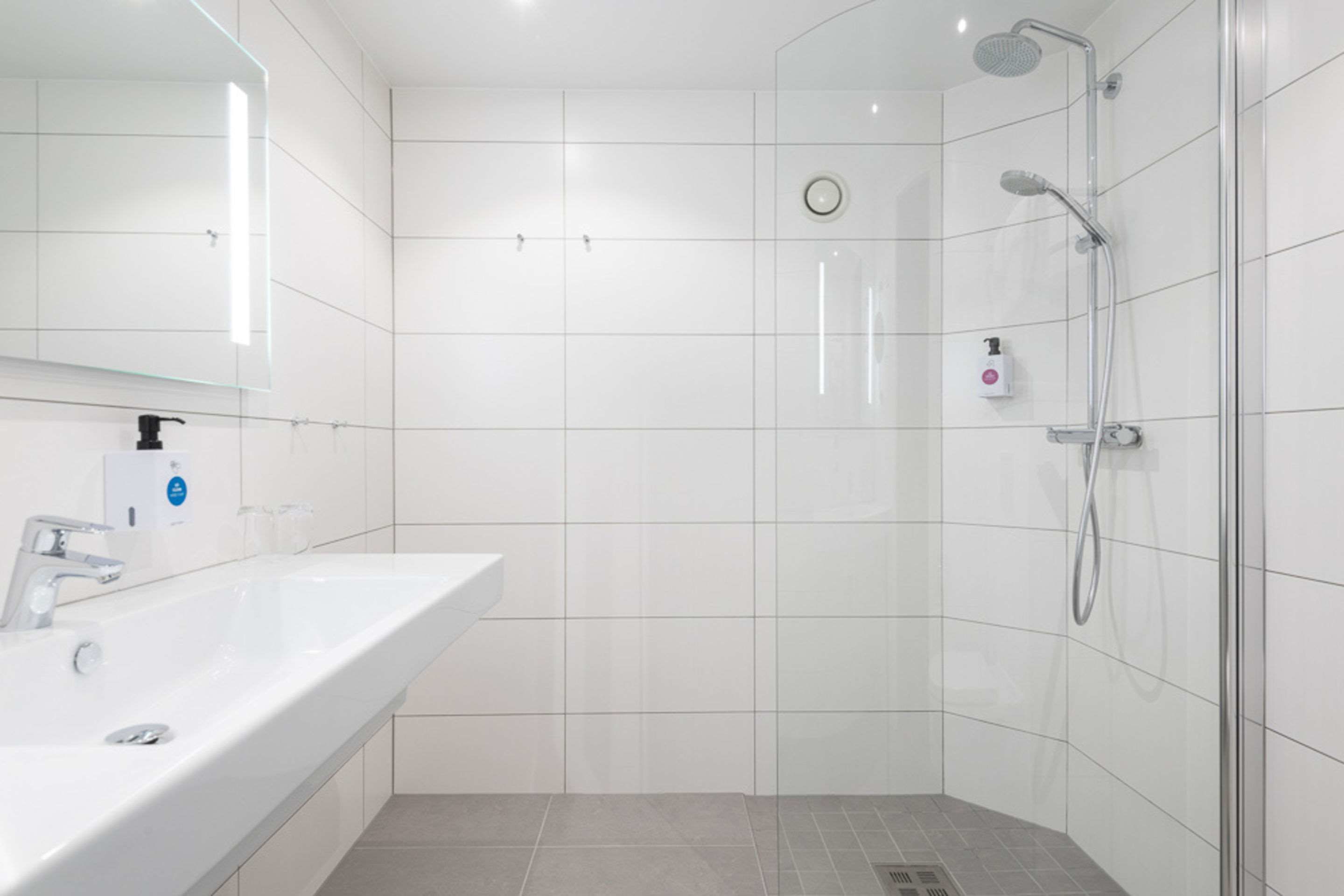Een moderne badkamer met een witte wastafel, spiegel en douche.