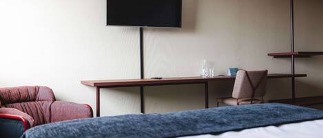 A hotel room with a bed, a desk, a chair, a television, and a small table with a glass and a bottle.