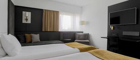 A hotel room with a large bed, a desk, a chair, a TV, and a window with curtains.