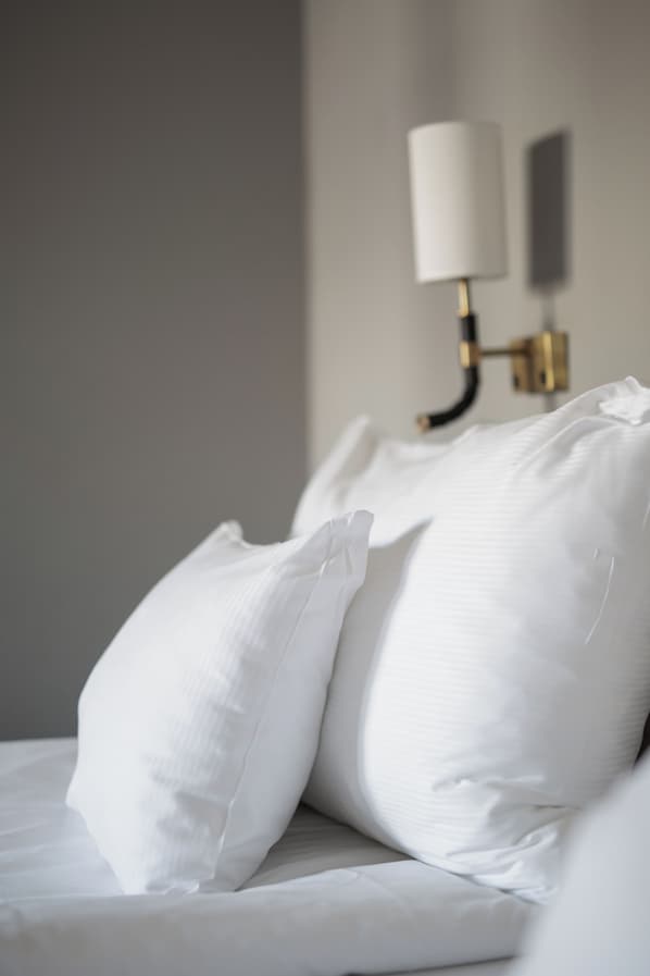 Una cama bien hecha con sábanas y almohadas blancas, una lámpara de pared y un diseño de habitación sencillo y limpio.