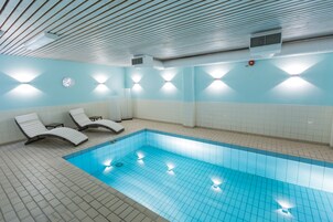 Una piscina interior con paredes y techo azulejados, dos sillones de descanso y luces fijadas a la pared.
