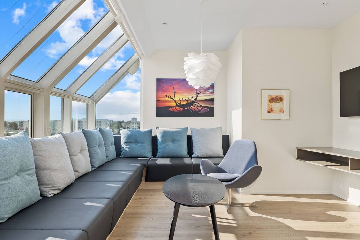 Ein modernes Wohnzimmer mit einer großen Couch, einem Essbereich und Blick auf die Stadt durch Dachfenster.