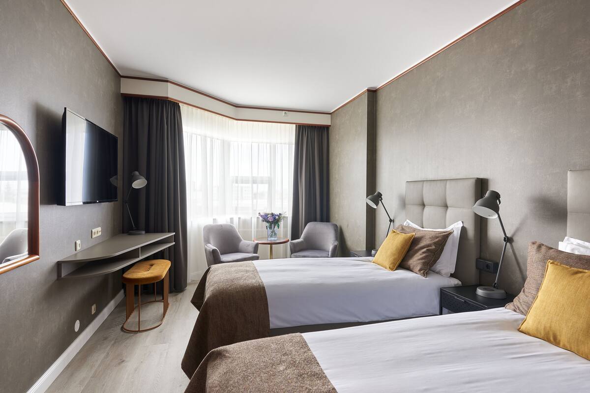 Ein modernes Hotelzimmer mit zwei Betten, einem Schreibtisch, einem Fernseher und Blick ins Freie.